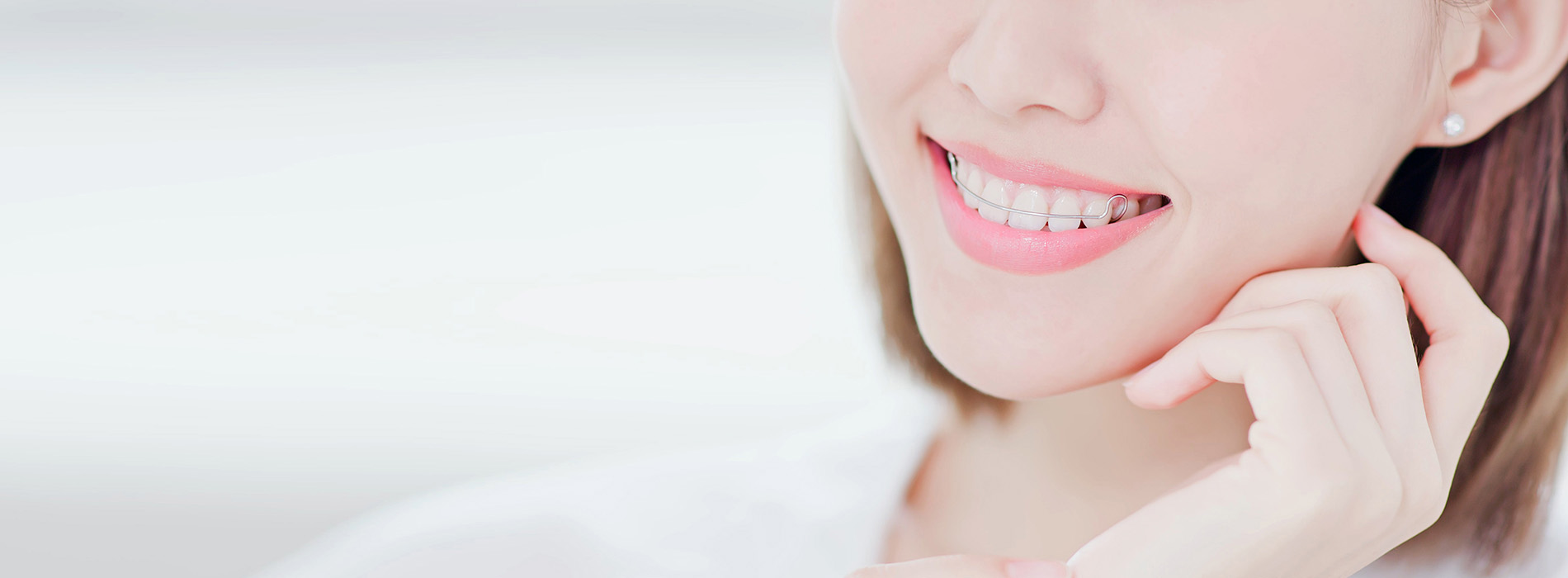 A smiling woman with short hair, wearing a white top, against a blurred background.