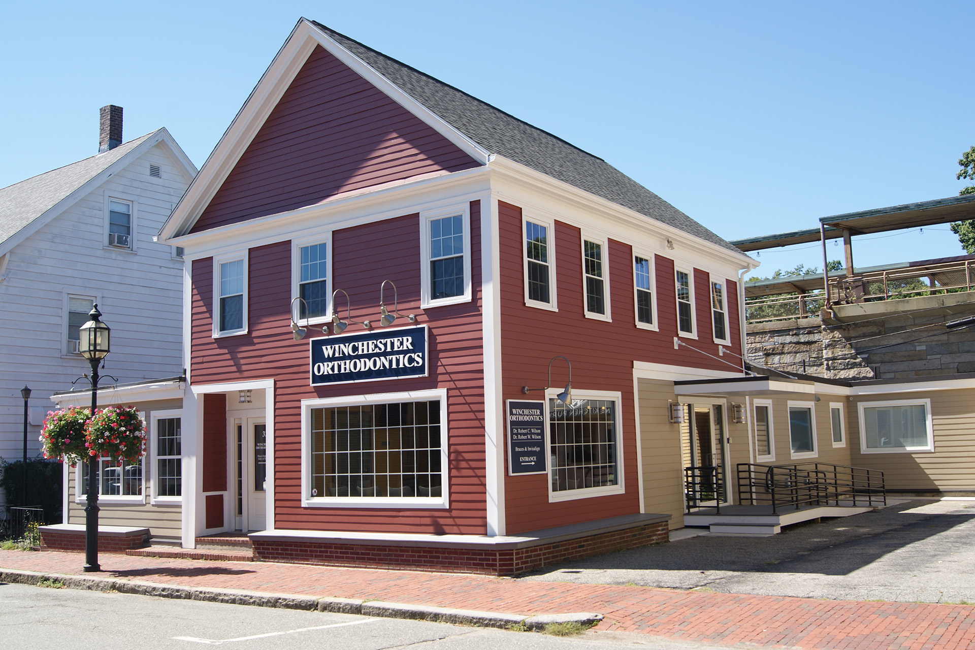 The image shows a red and white two-story building with a sign that reads  Woodstock Inn  on the front. It appears to be a small, quaint inn with a brick base, situated in a neighborhood setting with other similar buildings nearby.