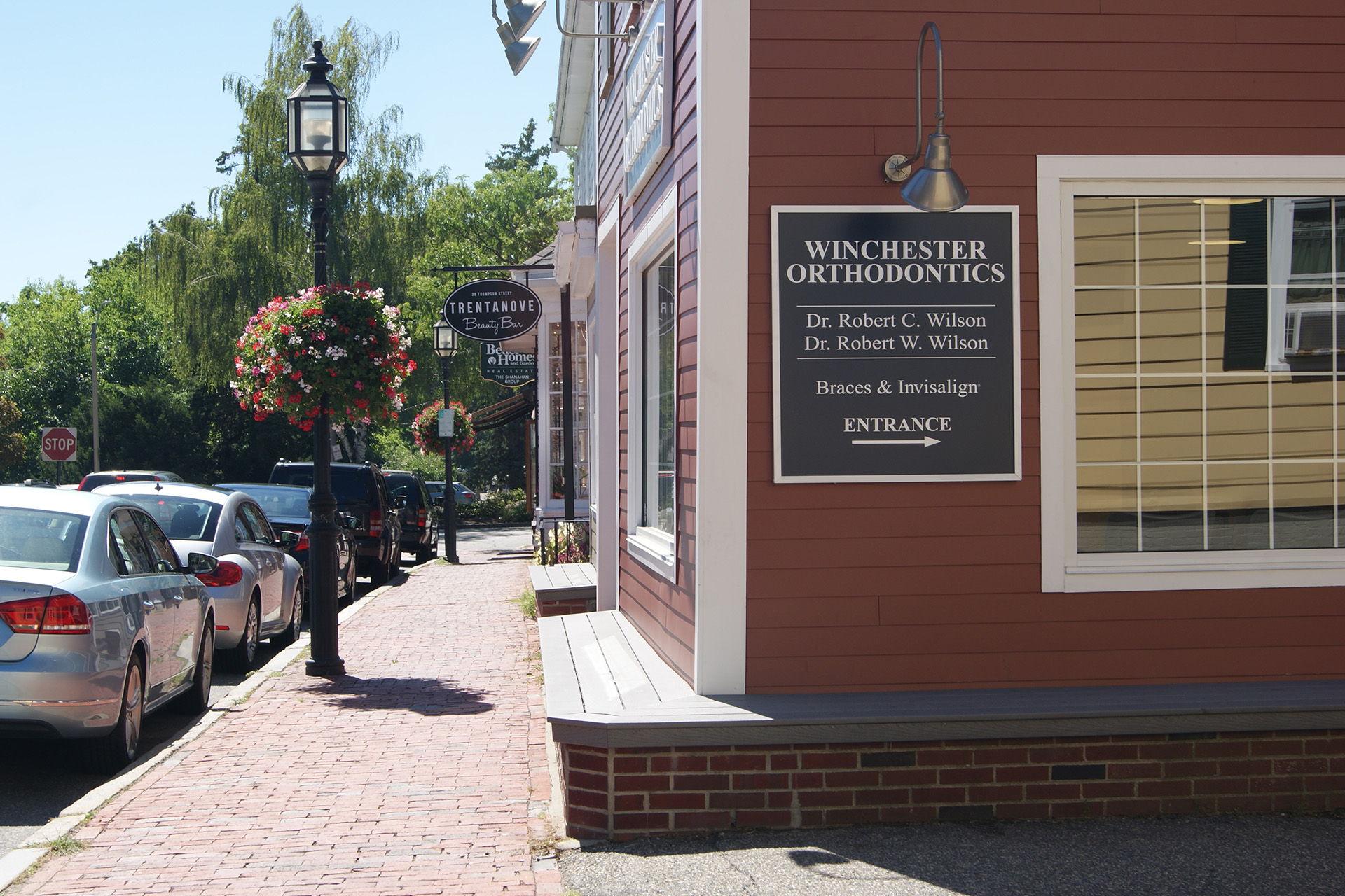 The image shows a red brick building with a sign that reads  WINESTON  and includes additional text, situated on a street corner with a sidewalk, parked cars, and a clear sky.