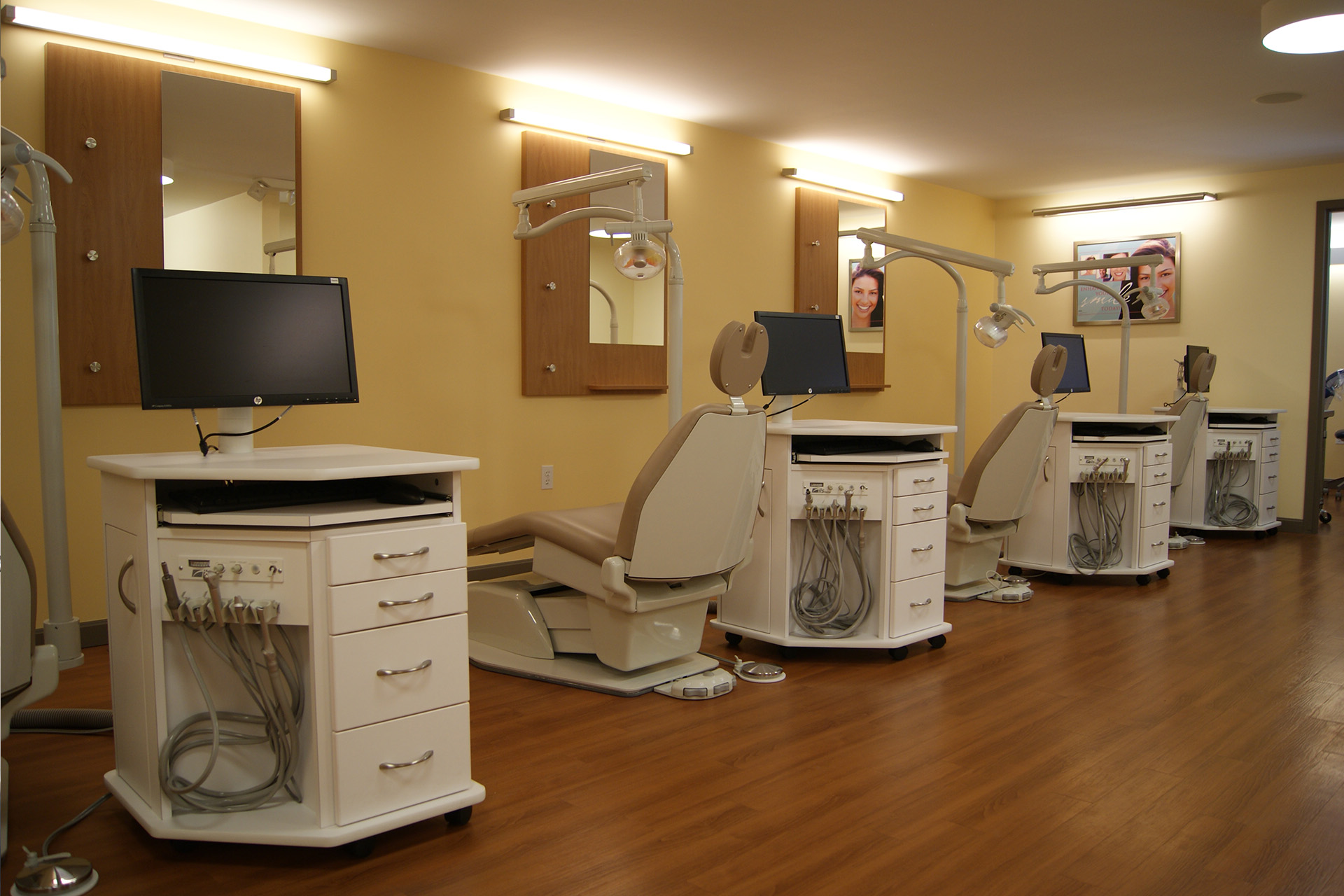 A well-lit dental office with multiple dental chairs, each equipped with a computer screen and other medical equipment.
