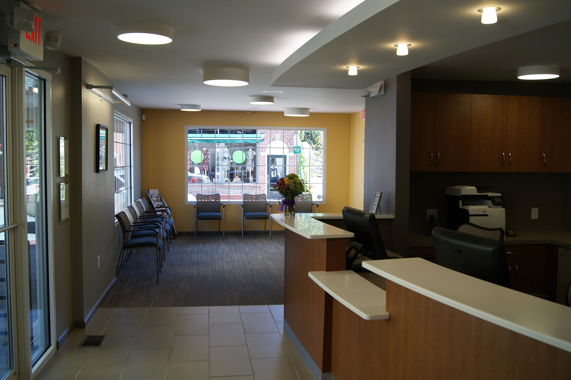 The image shows an interior view of a well-lit, modern office space with a reception area featuring a desk and chairs, a waiting area with seating, and a clean, contemporary design.