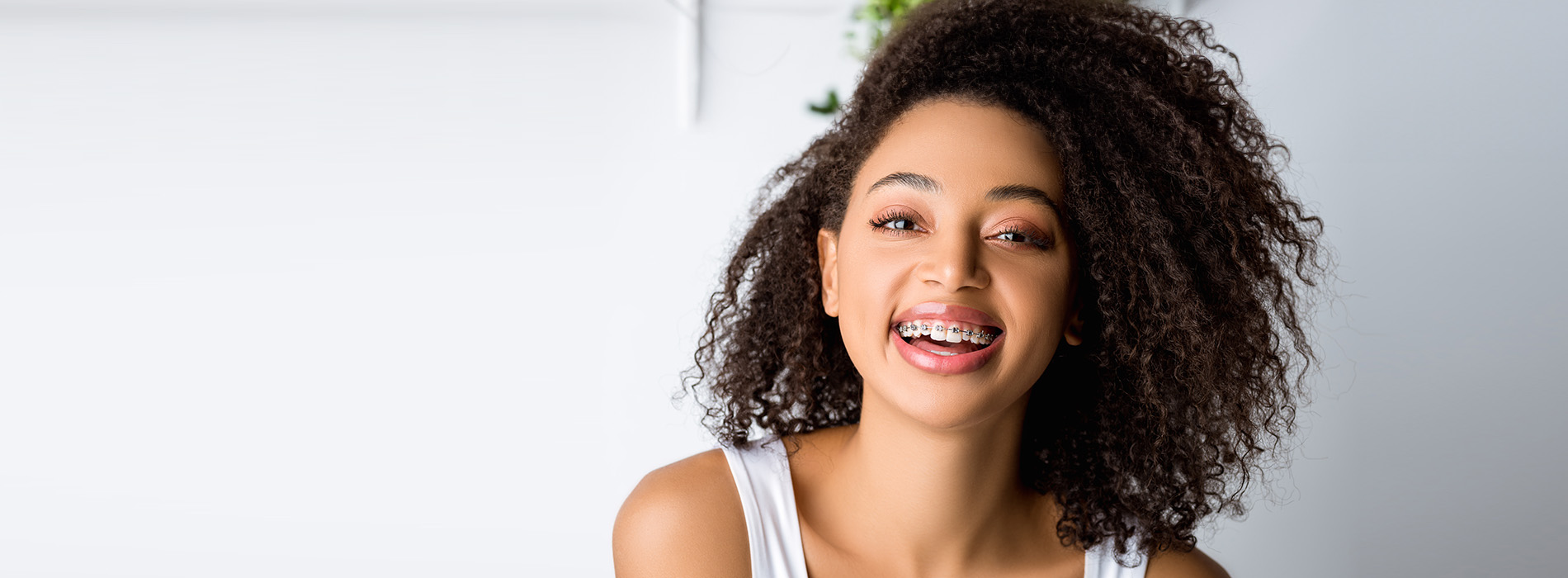 A young woman with a radiant smile, wearing a white top, stands against a light background.