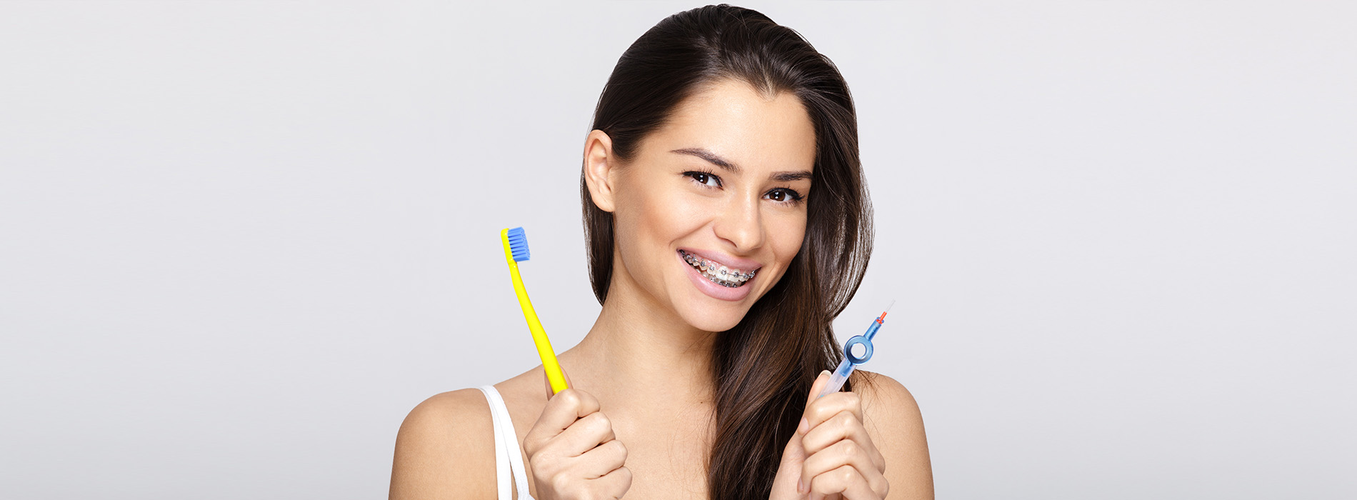 A young woman with a toothy grin is holding a toothbrush in her hand.