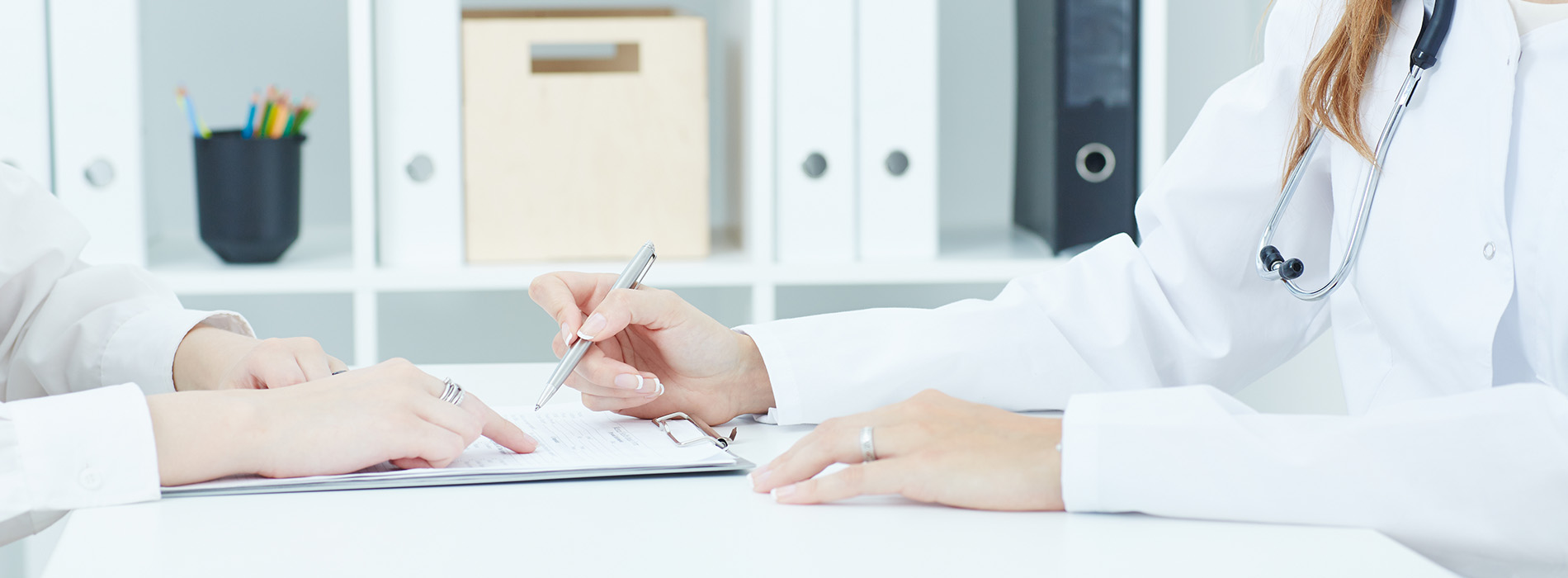 Two individuals, likely healthcare professionals, seated at a desk with papers and a pen, in a professional setting.