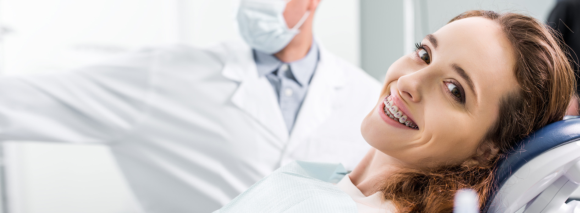 The image shows a woman in a dental office, sitting in a chair with her eyes closed and smiling, while a dentist is standing beside her, wearing a white coat and holding a mirror.