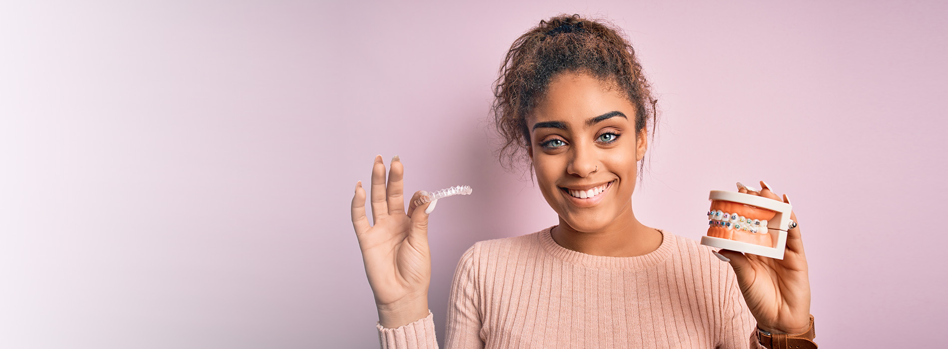 A woman is holding a toothpaste tube while standing against a pink background.