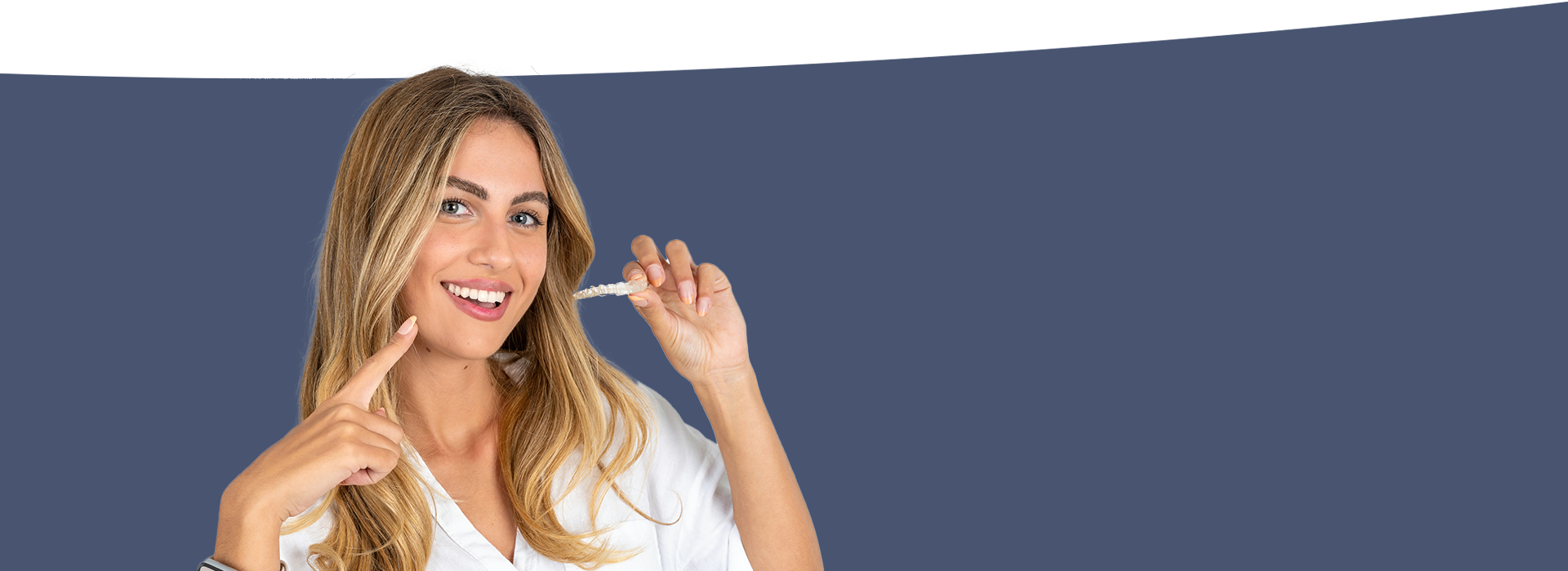 The image shows a woman with blonde hair, wearing a white shirt and holding a phone to her ear, smiling at the camera. She is standing against a blue background.